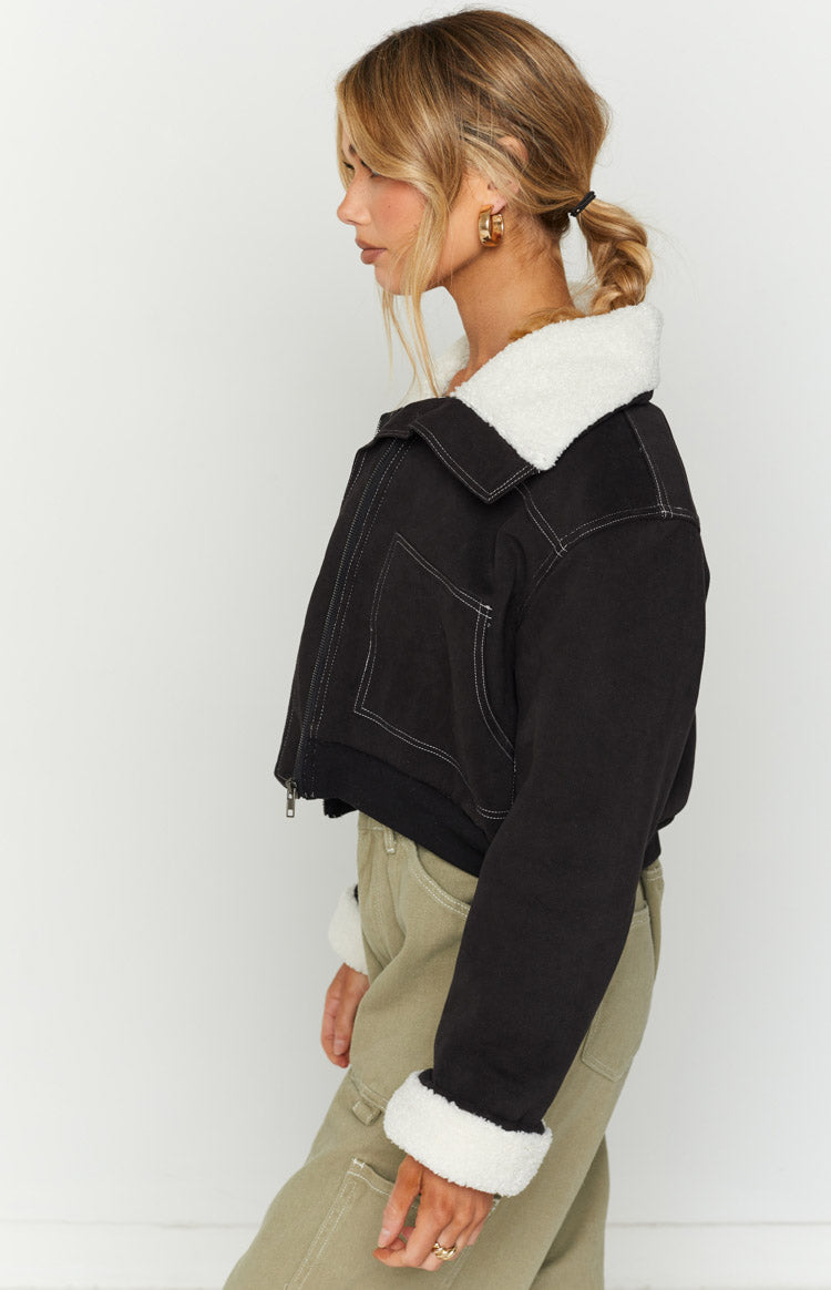 Side view of a black cropped denim sherpa jacket with white contrast stitching and rolled sherpa cuffs