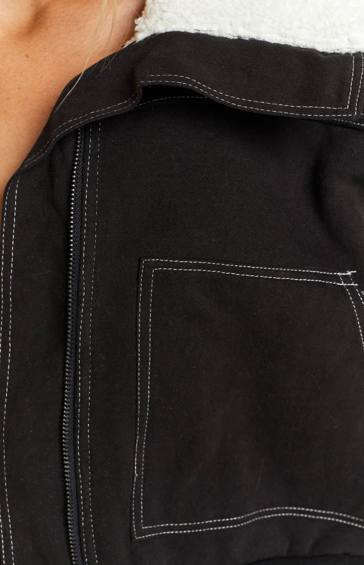 Close-up of black denim jacket with white sherpa collar, silver zipper, and white contrast stitching on chest pocket