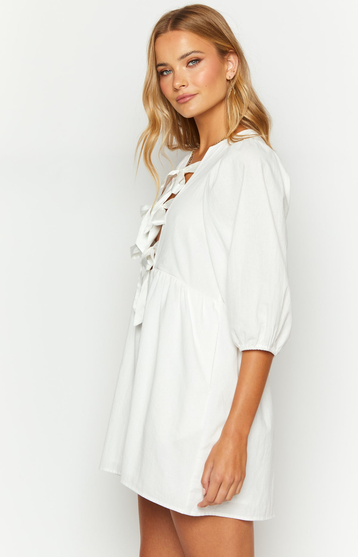 Side view of a white mini dress featuring a lace-up V-neckline with ties and 3/4 length puff sleeves with elasticated cuffs