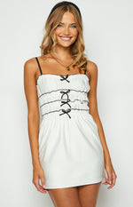 Close-up of the white mini dress bodice with black spaghetti straps, ruffled neckline, and three rows of black bows