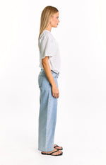 Side view of light wash denim low rise jeans with studded waistband and wide leg fit with raw hem