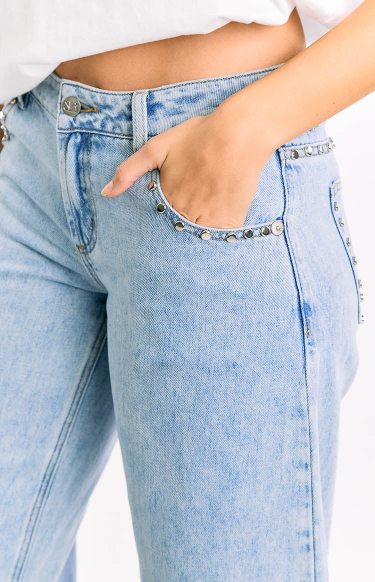 Close-up of the silver stud detail along the front pocket and side seam of light wash denim jeans