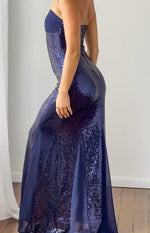 Side view of a navy sequin strapless maxi dress with a fitted silhouette and sheer fabric panels in the skirt