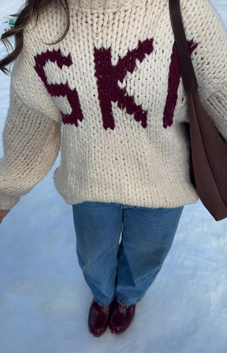 Cream chunky knit sweater with a burgundy "SKI" jacquard motif across the chest, showing the relaxed fit and ribbed hem