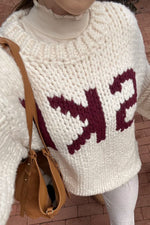 Close-up of a cream chunky knit sweater showing the textured knit and burgundy jacquard pattern