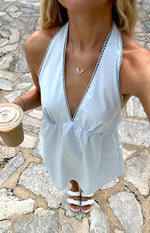 Top-down view of a light blue halter neck mini dress with a deep V-neck, scalloped trim, and gathered empire waist