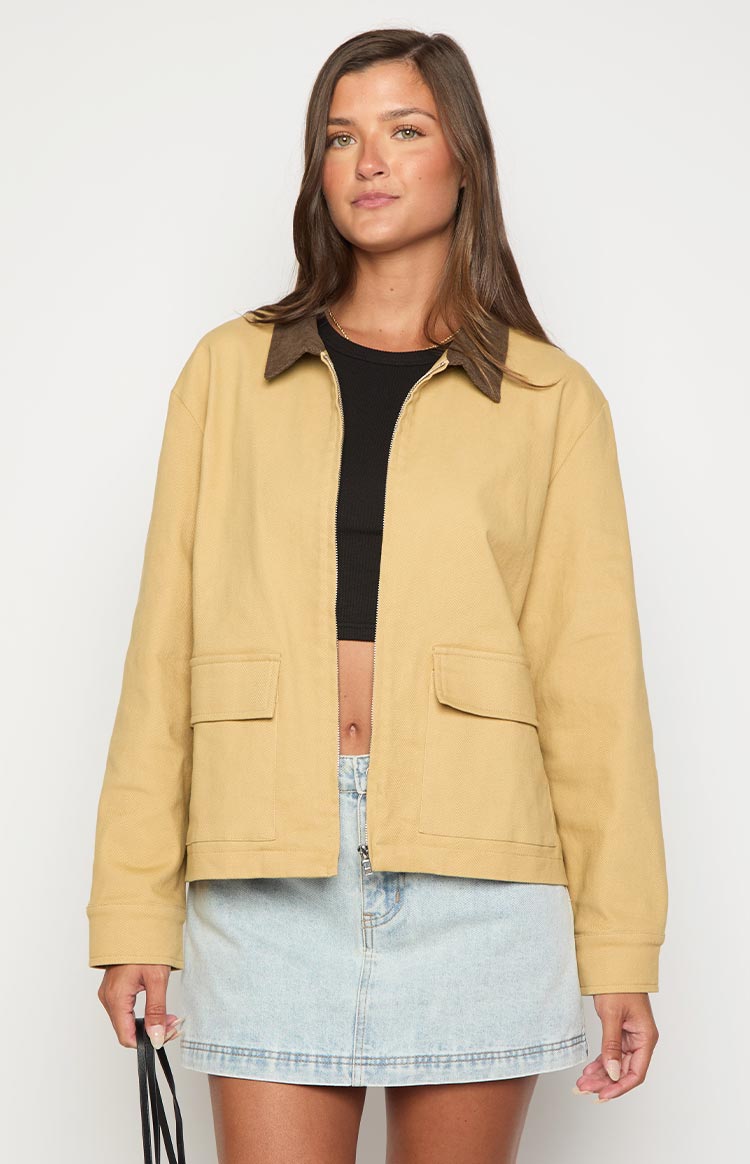 Tan canvas jacket with a brown contrast collar, partially open front zipper, and two flap pockets