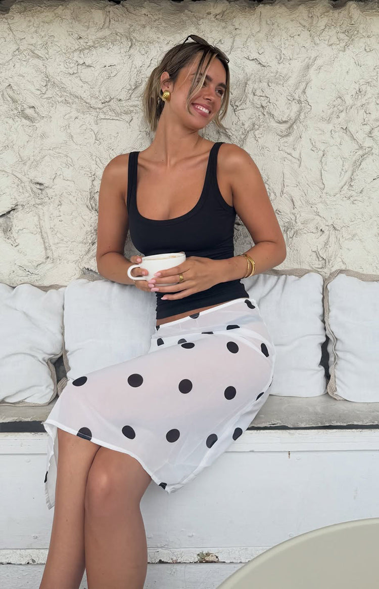 Side view of a white sheer midi skirt with black polka dots and an asymmetrical hemline