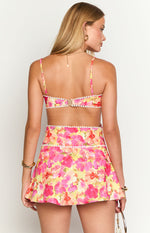 Rear view of the yellow floral mini dress with a hook-and-eye closure and white pom pom trim along the bodice and waist cut-out