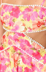 Close-up of the white pom-pom trim detailing the straight neckline and waist cutouts of the yellow floral mini dress