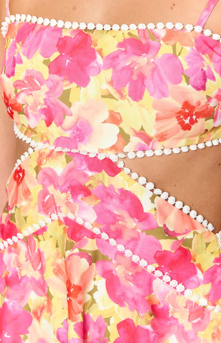 Close-up of the white pom-pom trim detailing the straight neckline and waist cutouts of the yellow floral mini dress