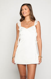 Front view of a white satin mini dress with ruffled shoulder straps and side ruffles
