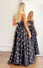 Rear view of a black polka dot strapless satin maxi dress with a fitted bodice and full flowing skirt