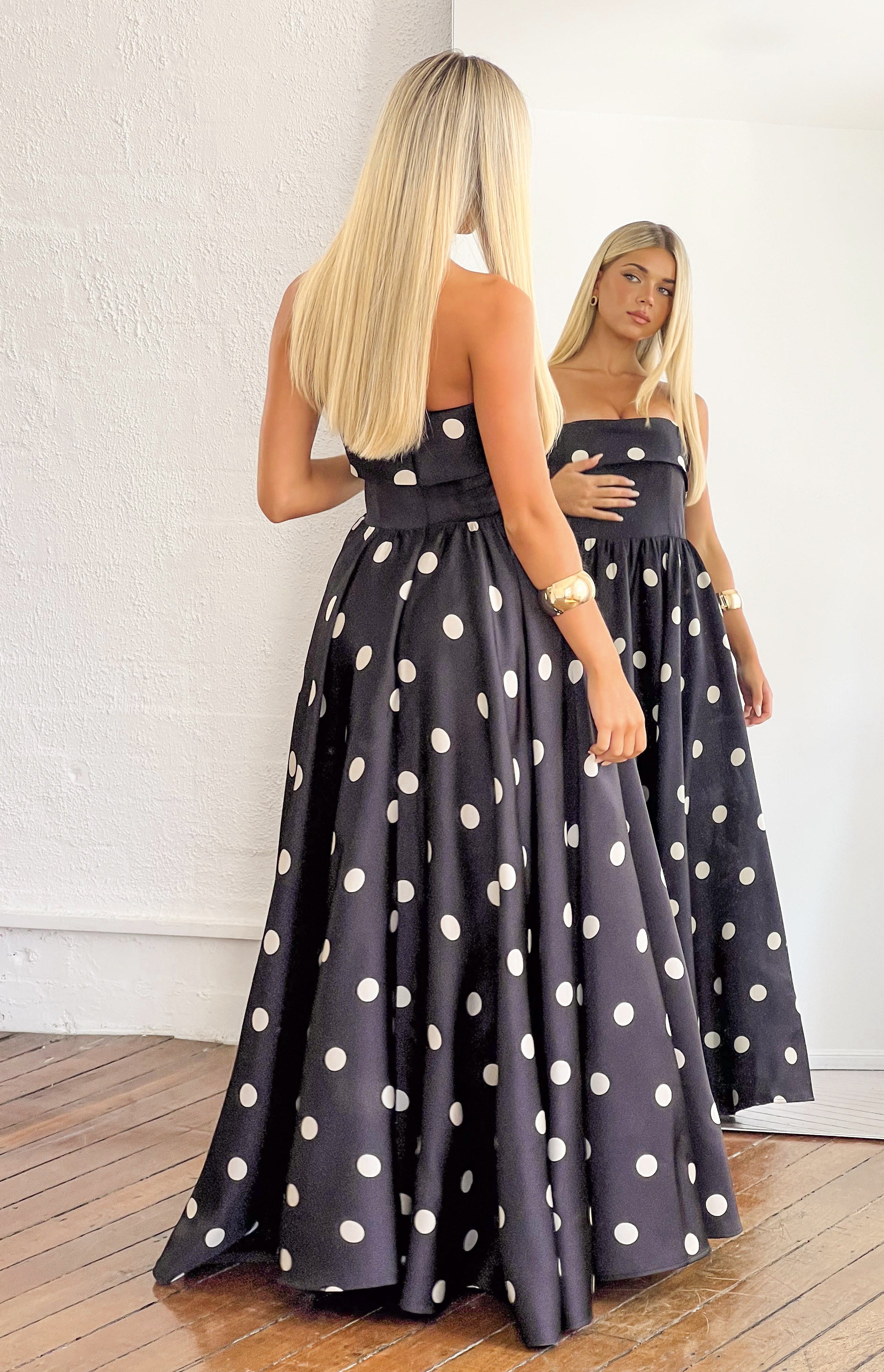 Rear view of a black polka dot strapless satin maxi dress with a fitted bodice and full flowing skirt