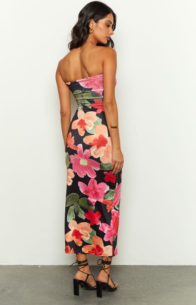 Front view of a black floral midi dress with a twisted strapless bust, midriff cutout, and ruched bodycon skirt