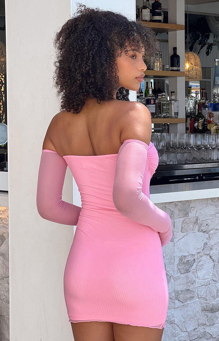 Rear-side view of a pink ribbed off-shoulder mini dress, showing the sheer long sleeves and bodycon fit