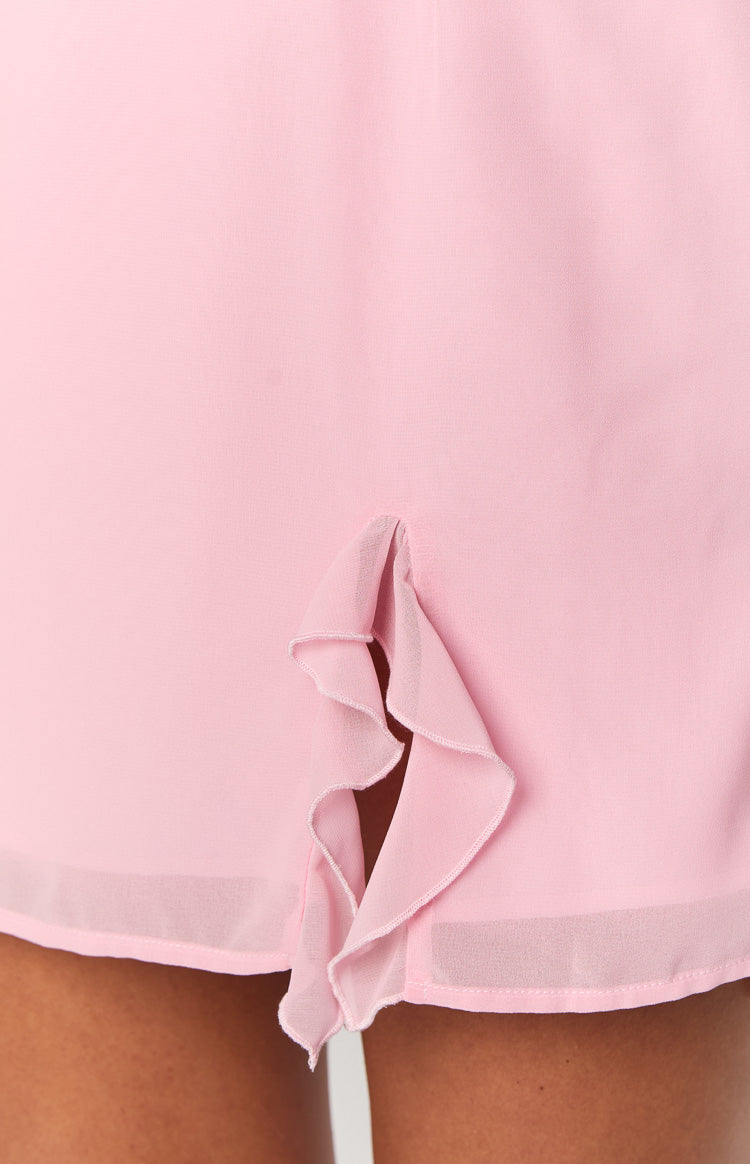 Close-up of the ruffled side slit detail on the hem of a pink mini dress, showing the sheer overlay