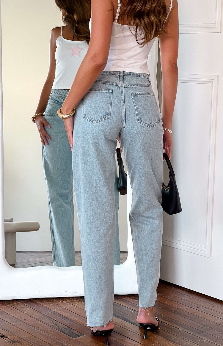 Rear view of light blue high-waisted jeans with back pockets, a straight leg, and frayed hem