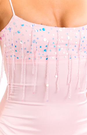 A close-up view of our model showing a pale pink mini dress with a satin-like finish. This top of the dress has a fringe of pink beads and iridescent sequins hanging from it.