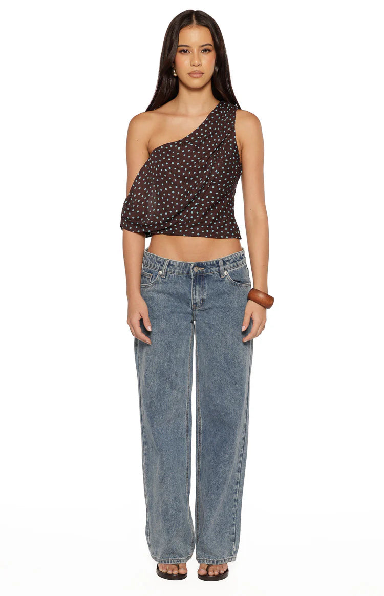 Front view of a brown one-shoulder polka dot crop top with a flowy sleeve and fitted hem
