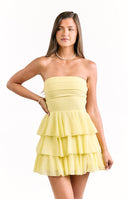 A model wearing a pale yellow strapless mini dress with a fitted ruched bodice and a tiered ruffled skirt.