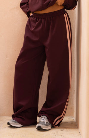 Close up of burgundy wide leg track pants with light pink side stripes comfortable for lounging or travel