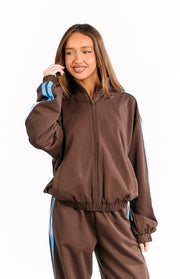 Front view of a chocolate brown zip-front jacket with a stand collar, blue sleeve stripes, and elasticated hem