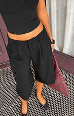 Close-up of black tailored culottes showing front pleats, belt loops, and side pockets