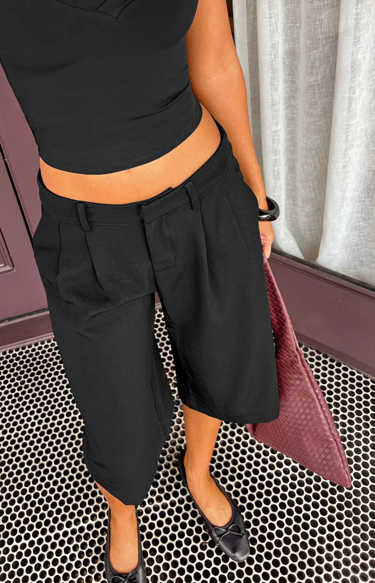 Close-up of black tailored culottes showing front pleats, belt loops, and side pockets