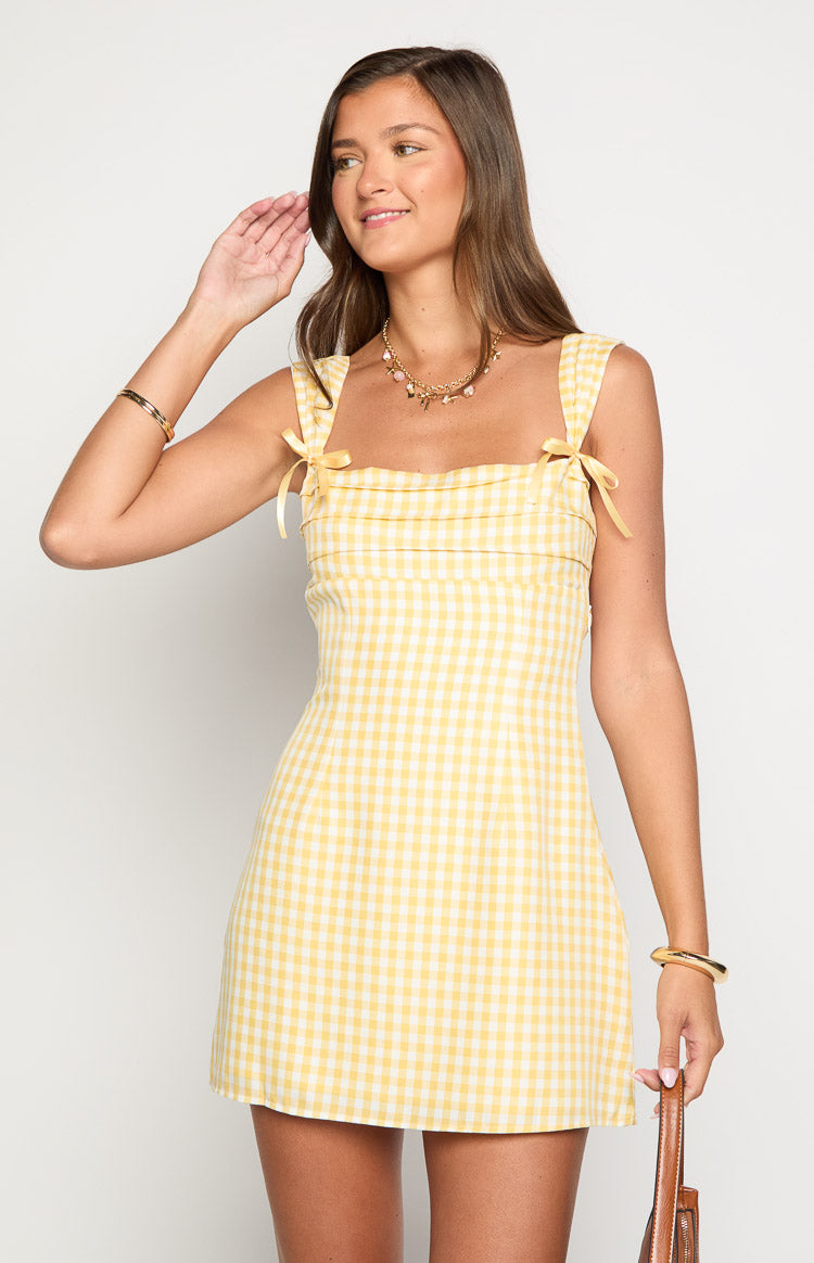 Front view of a yellow gingham mini dress with a square neckline, tie-up shoulder straps, and gathered bodice detail