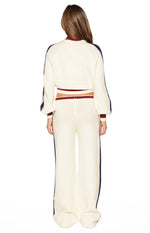 Rear view of a cream knit cropped sweater with red trim and blue stripes, paired with wide-leg pants with blue stripes