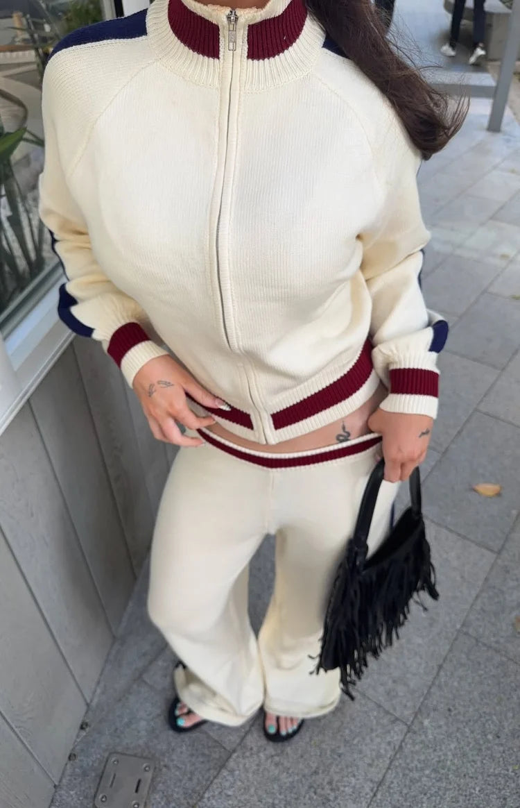 Cream knit zip sweater with burgundy and navy striped collar, cuffs, and hem, paired with matching wide-leg pants with a burg