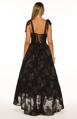 Rear view of a black maxi dress with tie shoulders, a corset lace-up back, and a sheer floral overlay skirt