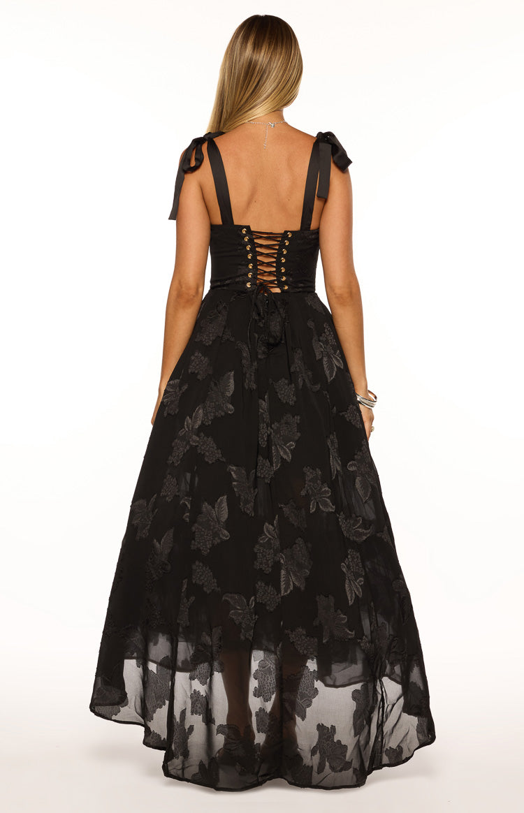 Rear view of a black maxi dress with tie shoulders, a corset lace-up back, and a sheer floral overlay skirt