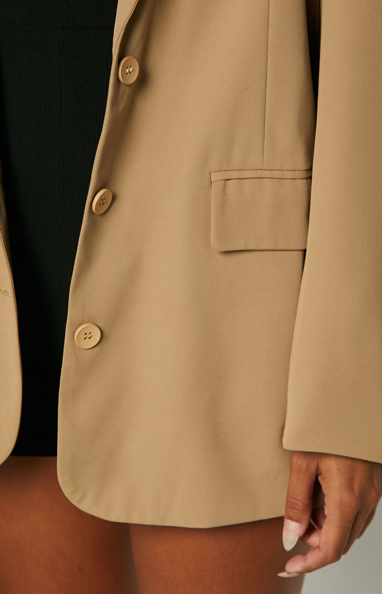 Detail shot of the tan blazer featuring two light brown buttons on the placket and a flap pocket