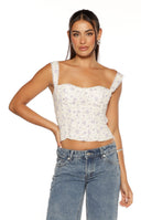 A sleeveless white corset-style top with a small purple floral print featuring a sweetheart neckline in a smocked bodice and wide ruffled lace shoulder straps.