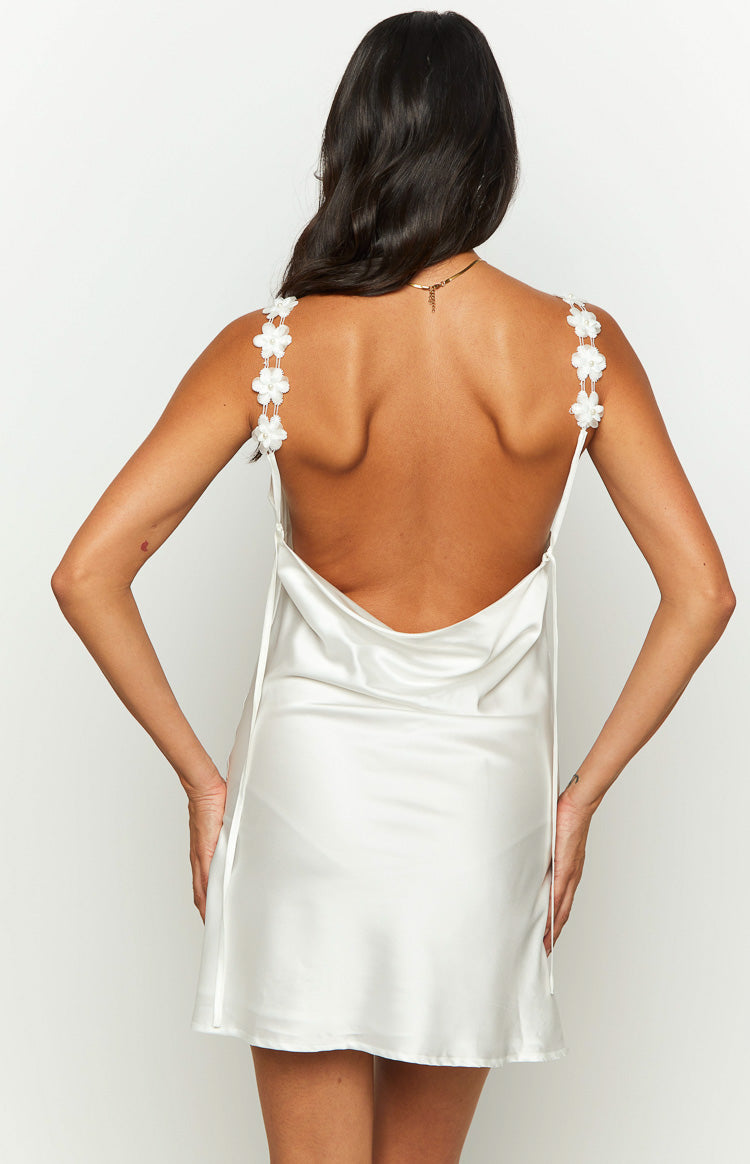 Rear view of a white satin mini dress featuring a low cowl back and delicate spaghetti straps with floral appliques