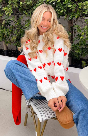 White knitted jumper with red heart patterns on the body and sleeves, featuring a crew neck and ribbed cuffs