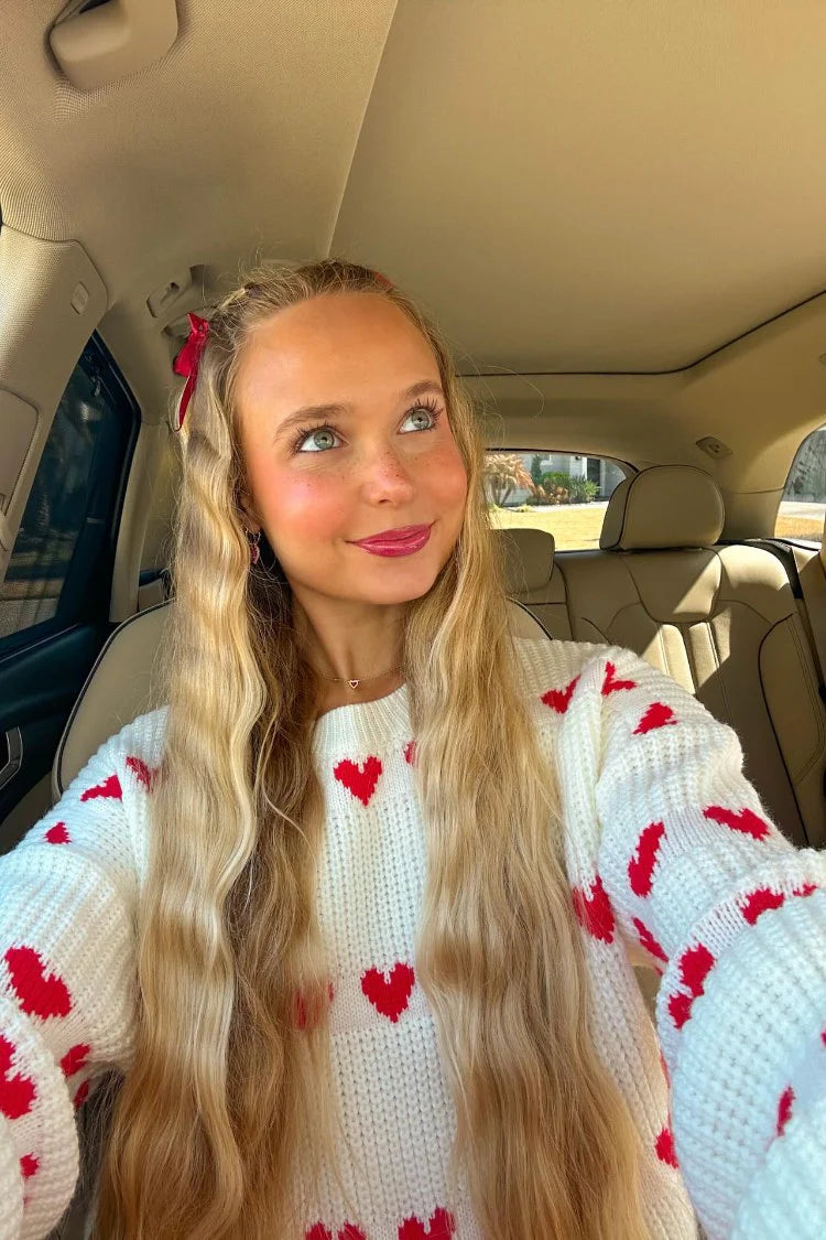 Close-up of a white chunky knit jumper with red heart pattern and round neckline