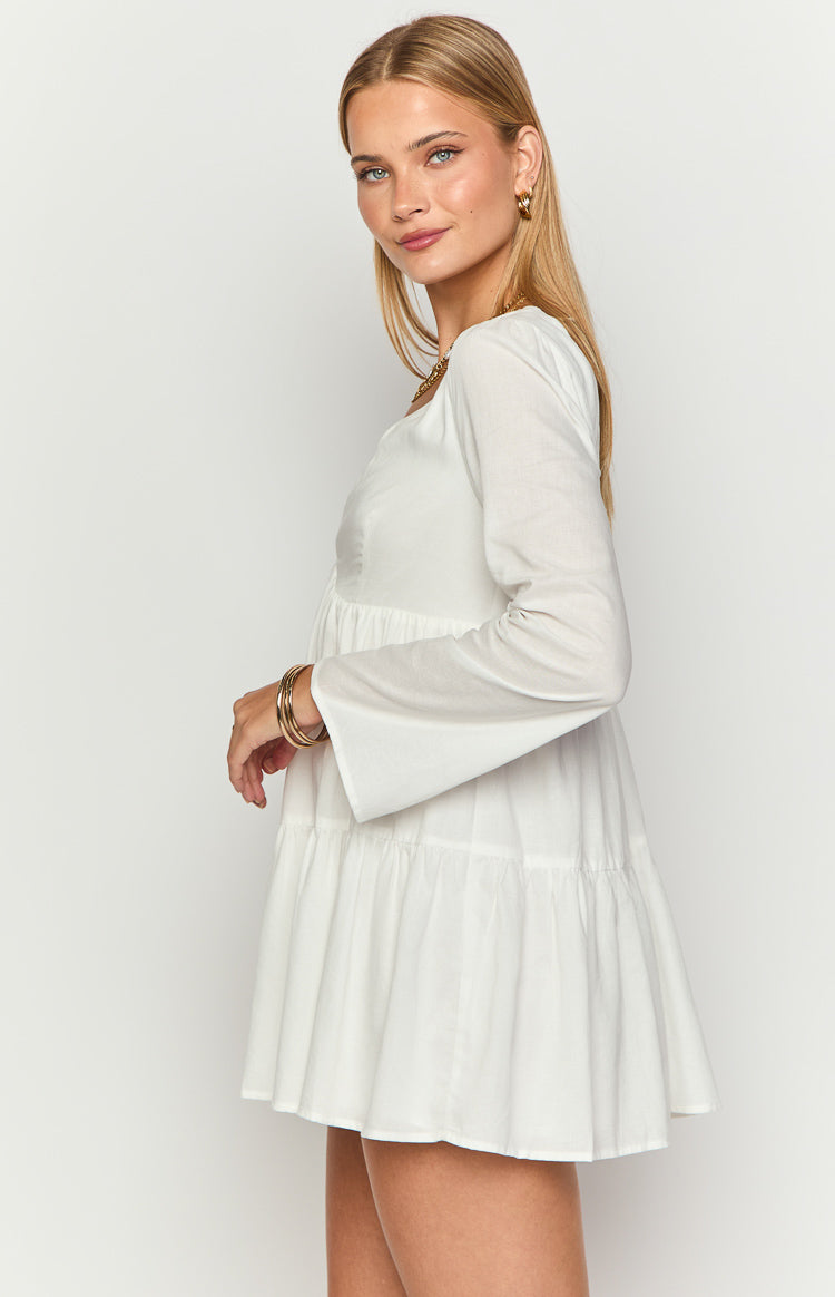 Side view of a white long sleeve mini dress with a square neckline, tiered skirt, and flared cuffs