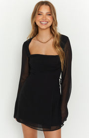 Close-up of the square neckline and ruched bust detail of a black mini dress with sheer long sleeves