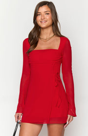 Red mini dress with square neckline, ruched bust, sheer long sleeves, and side tie detail