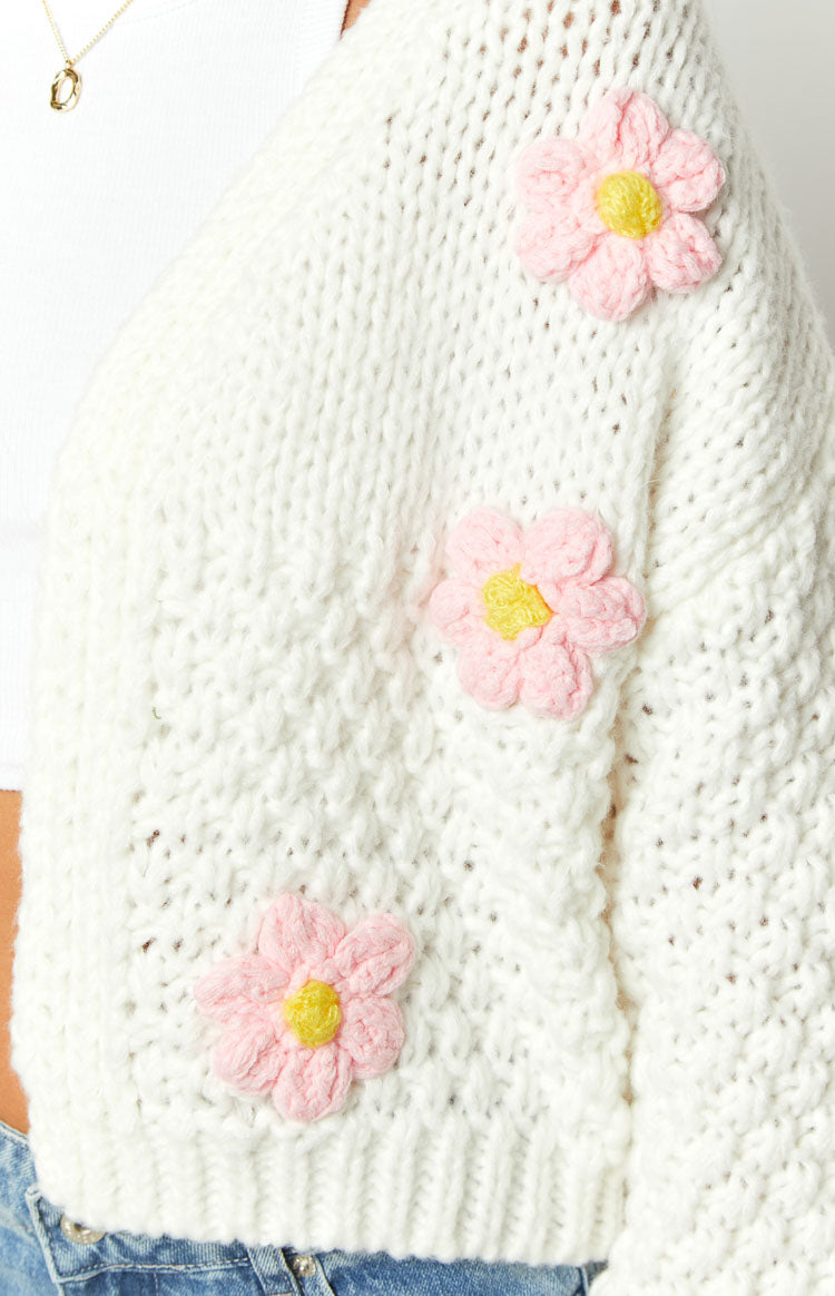 Side view of a white chunky knit cardigan with dropped shoulder and pink flower appliques
