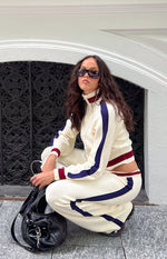 Side view of cream knit jacquard track pants, showing the relaxed fit, dark blue side stripe, and ribbed ankle cuffs