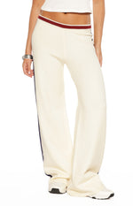 Close-up of cream knit track pants with a red and white ribbed waistband and dark blue side stripe
