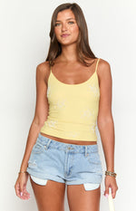 Front view of a yellow camisole top with white beaded floral patterns and thin spaghetti straps