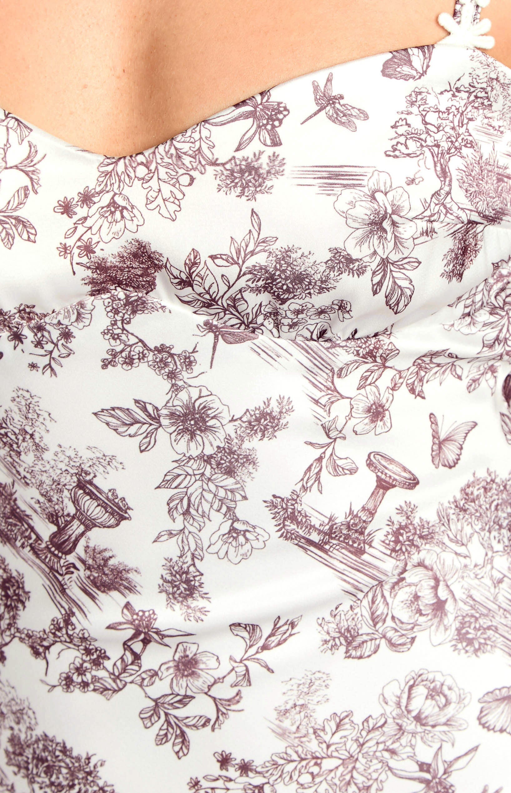 Close-up of the white satin fabric with a brown toile garden print featuring flowers, butterflies, and watering cans
