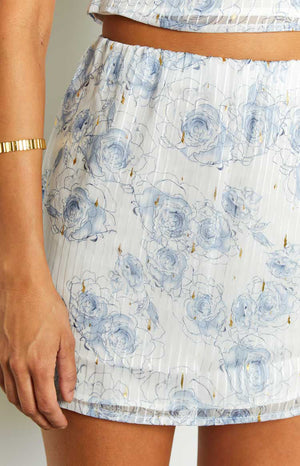 Close-up of the elasticated waist and white mini skirt fabric with blue rose print, gold flecks, and subtle vertical texture