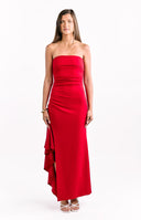 A female model wearing a red strapless maxi dress with a ruched bodice and a ruffled train or cascade detail on the side of the skirt.