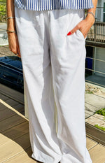 Close-up of white linen blend pants showing the elasticated waist, side pockets, and wide-leg drape